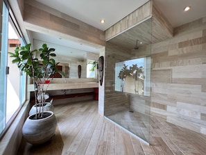 A modern bathroom with a large mirror, wooden flooring, and a potted plant.