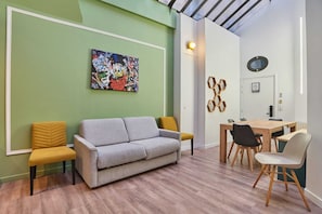 Um quarto com sofá cinzento, poltronas amarelas, mesa de jantar de madeira com cadeiras, parede verde e teto com claraboia.