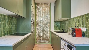 A compact kitchen with green cabinets, a washing machine, and a coffee machine. - Meslay 1 - Three Bedroom Apartment, Sleeps 8 (Paris)