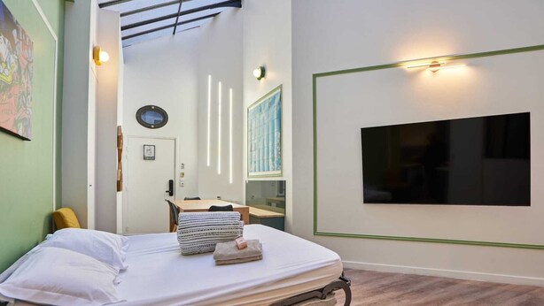 A bedroom with a bed, a desk, a chair, a window, and a wall-mounted TV. - Meslay 1 - Three Bedroom Apartment, Sleeps 8 (Paris)