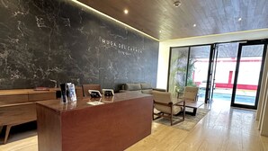 Un espace d’accueil moderne avec un mur en marbre, un comptoir d’accueil en bois et un coin salon comprenant un canapé et des fauteuils.