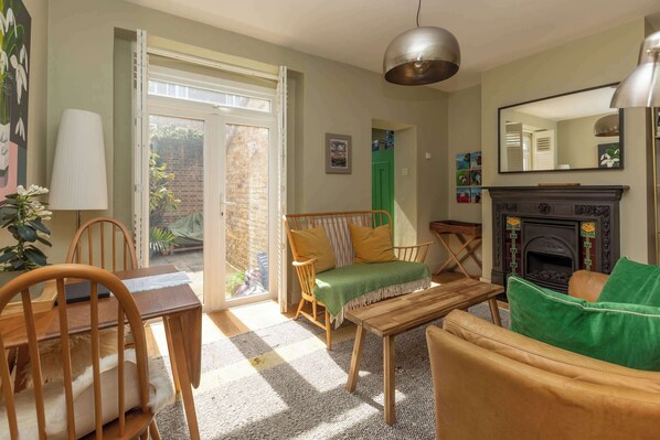 A living room with a fireplace, a dining area with a table and chairs, a sofa, and a large window with a view of the outside.