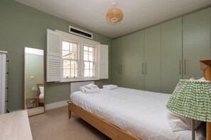 A bedroom with a bed, a bedside table, a lamp, a window with shutters, and a wardrobe.