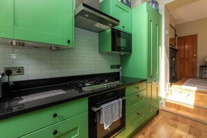 Uma cozinha com armários verdes, bancada preta, fogão e micro-ondas.