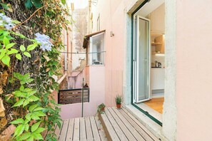 A narrow wooden deck with potted plants, a glass door leading to a kitchen, and a wall-mounted window.