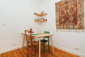 A dining area with a wooden table, two chairs, a patterned rug, and wall-mounted shelves.