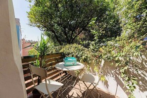 Een terras met een tafel en stoelen, omringd door weelderige begroeiing en een grote boom.