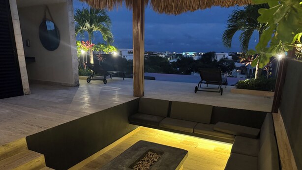 An outdoor seating area with a fire pit, cushioned benches, and a staircase leading to an upper level. - Penthouse Retreat w/Private Rooftop Pool (Tulum)