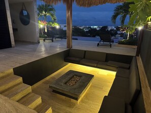 An outdoor seating area with a fire pit, cushioned benches, and a staircase leading to an upper level. - Penthouse Retreat w/Private Rooftop Pool (Tulum)
