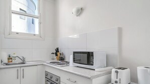 Een moderne keuken met witte kasten, een magnetron, een broodrooster en een spoelbak.