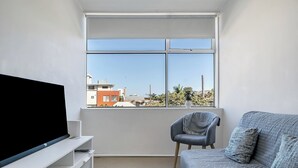 Een moderne woonkamer met een groot raam, een flatscreen televisie, een grijze bank en een fauteuil.
