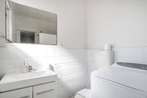 A modern bathroom with white fixtures, a mirror, a toilet, and a built-in heater.