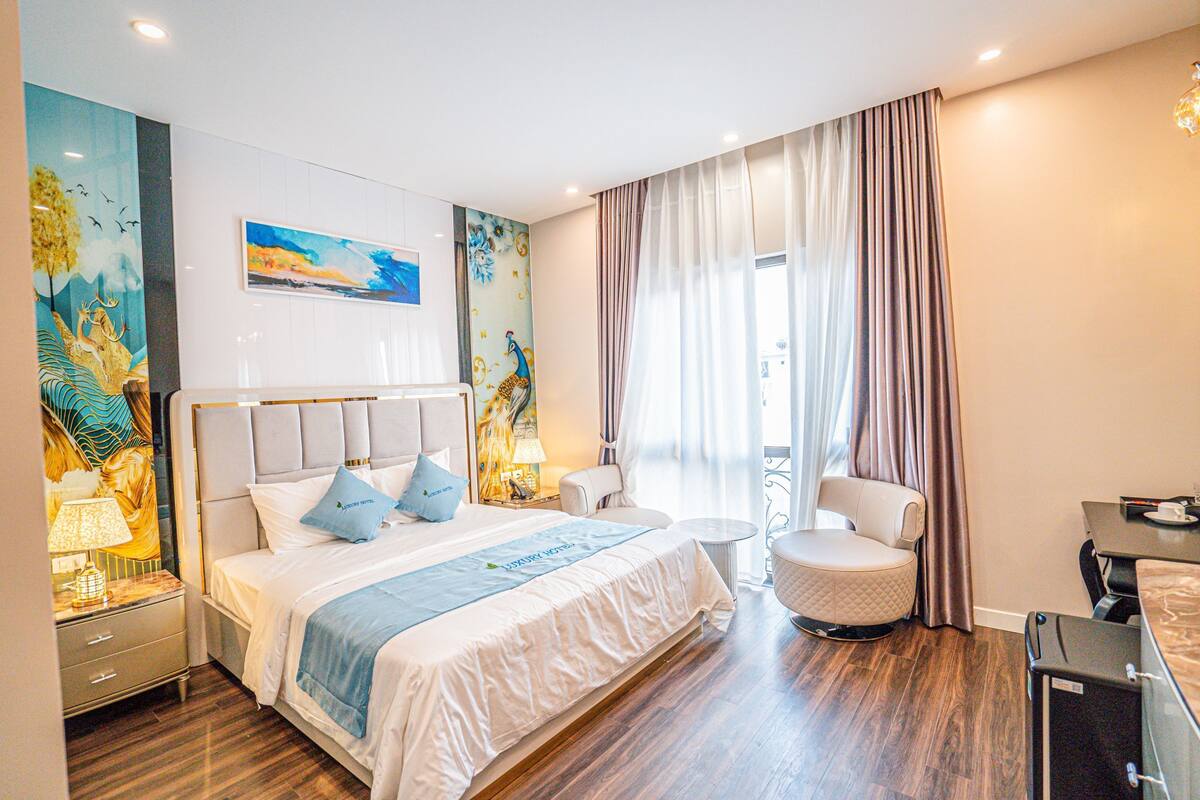 A hotel room with a large bed, a chair, a small table, and a desk.
