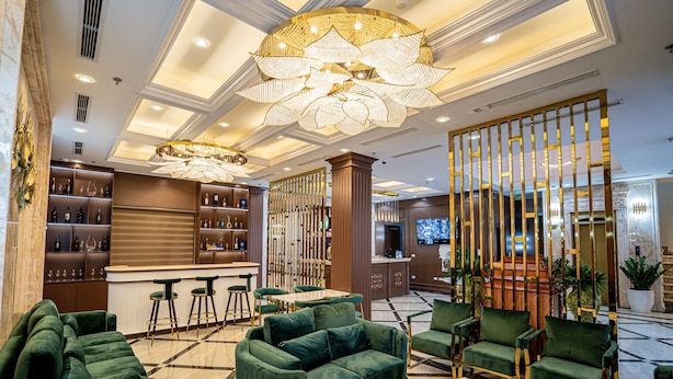 A lobby with green sofas, a bar area, and a television screen. - Luxury Hotel (Van Giang)