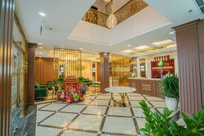 A hotel lobby with a reception desk, seating area, and decorative plants. - Luxury Hotel (Van Giang)