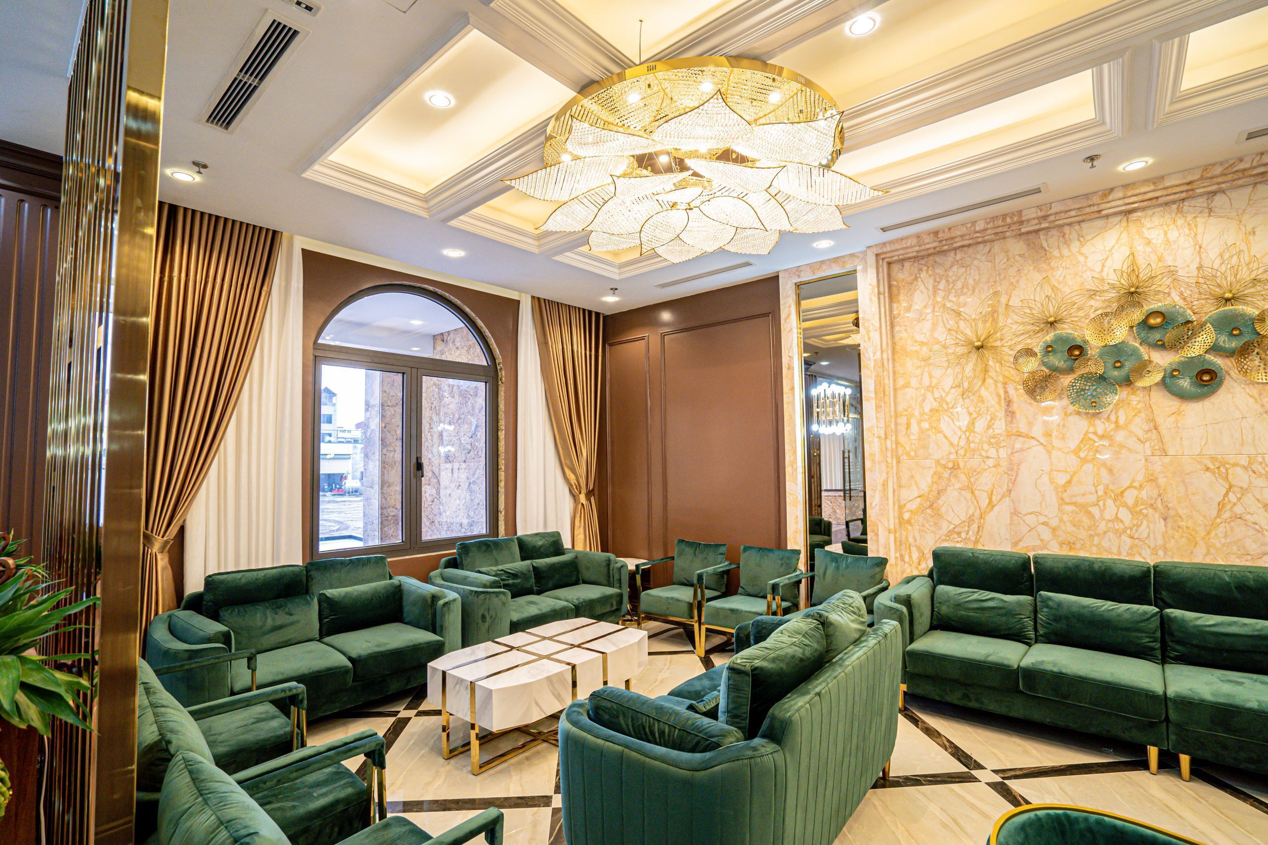A spacious lobby with green sofas, a central coffee table, and a decorative chandelier.
