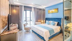 A modern hotel room with a large bed, a television, a seating area, and a painting on the wall. - Luxury Hotel (Van Giang)