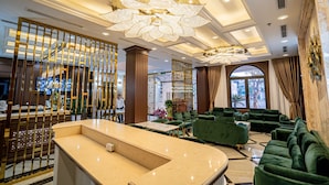 A lobby with a reception desk, green sofas, a large chandelier, and a view through the window. - Luxury Hotel (Van Giang)