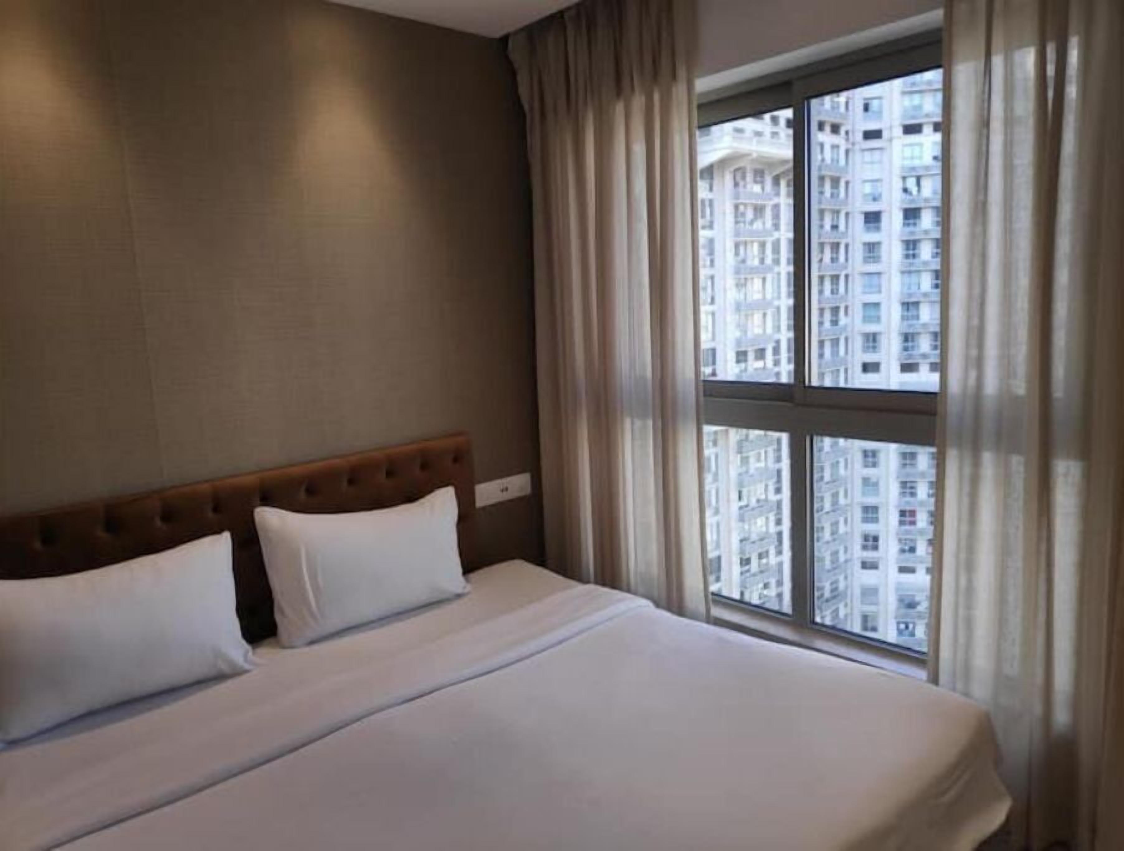 Quarto de hotel com uma cama grande, cabeceira e janela com cortinas.