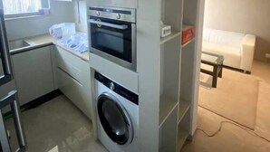 Cocina compacta con electrodomésticos integrados, lavadora y un pequeño comedor con un sofá blanco.