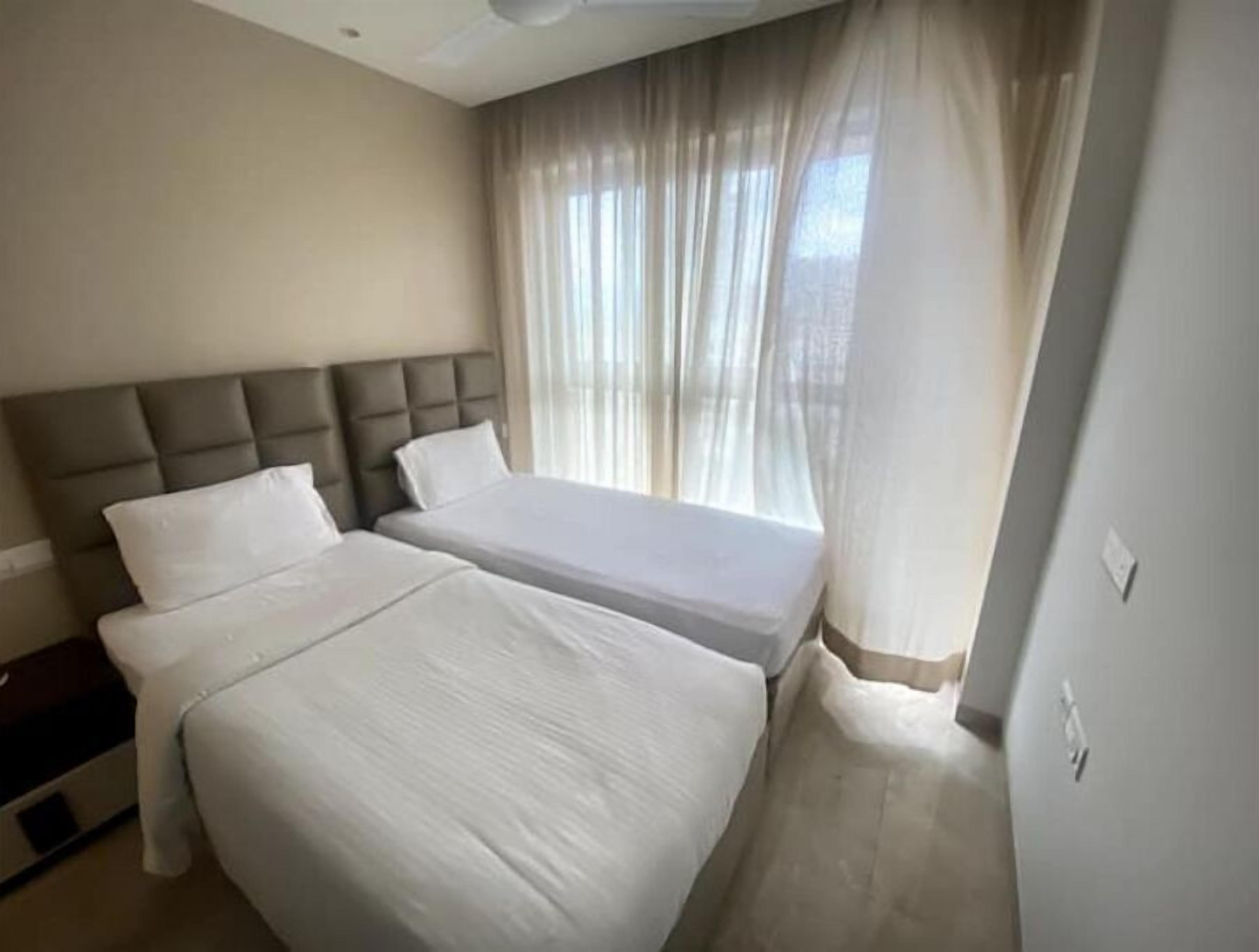 Une chambre d’hôtel avec deux lits, une tête de lit et une fenêtre ornée de rideaux légers.