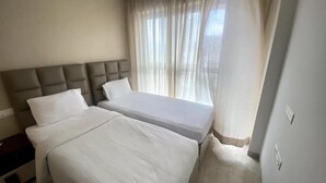 Habitación de hotel con dos camas, cabecera y ventana con cortinas traslúcidas.