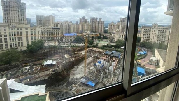 Vista desde una ventana con una construcción a la vista y edificios al fondo.
