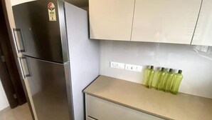 Una cocina con un refrigerador de acero inoxidable, una encimera color crema y un juego de botellas verdes.