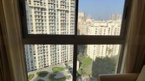 Quarto com uma janela ampla com vista para uma área residencial com edifícios altos.