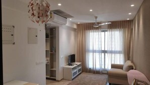 Uma sala de estar moderna com um sofá, uma TV e uma mesinha. Há um ventilador de teto, uma janela com cortinas e uma estante embutida.
