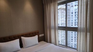 Quarto de hotel com uma cama grande, cabeceira e janela com cortinas.