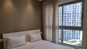 A hotel room with a large bed, a view of a high-rise building, and a window with curtains. - Luxurious budget stay in Powai (Ocean Heights)