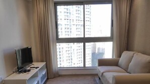 A living room with a sofa, a TV on a stand, a window with curtains, and a view of high-rise buildings. - Luxurious budget stay in Powai (Ocean Heights)