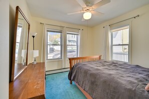 Quarto com cama, cômoda, ventilador de teto e janelas amplas.