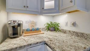A kitchen with white cabinets, a coffee maker, a tray with coffee cups, and a potted plant.