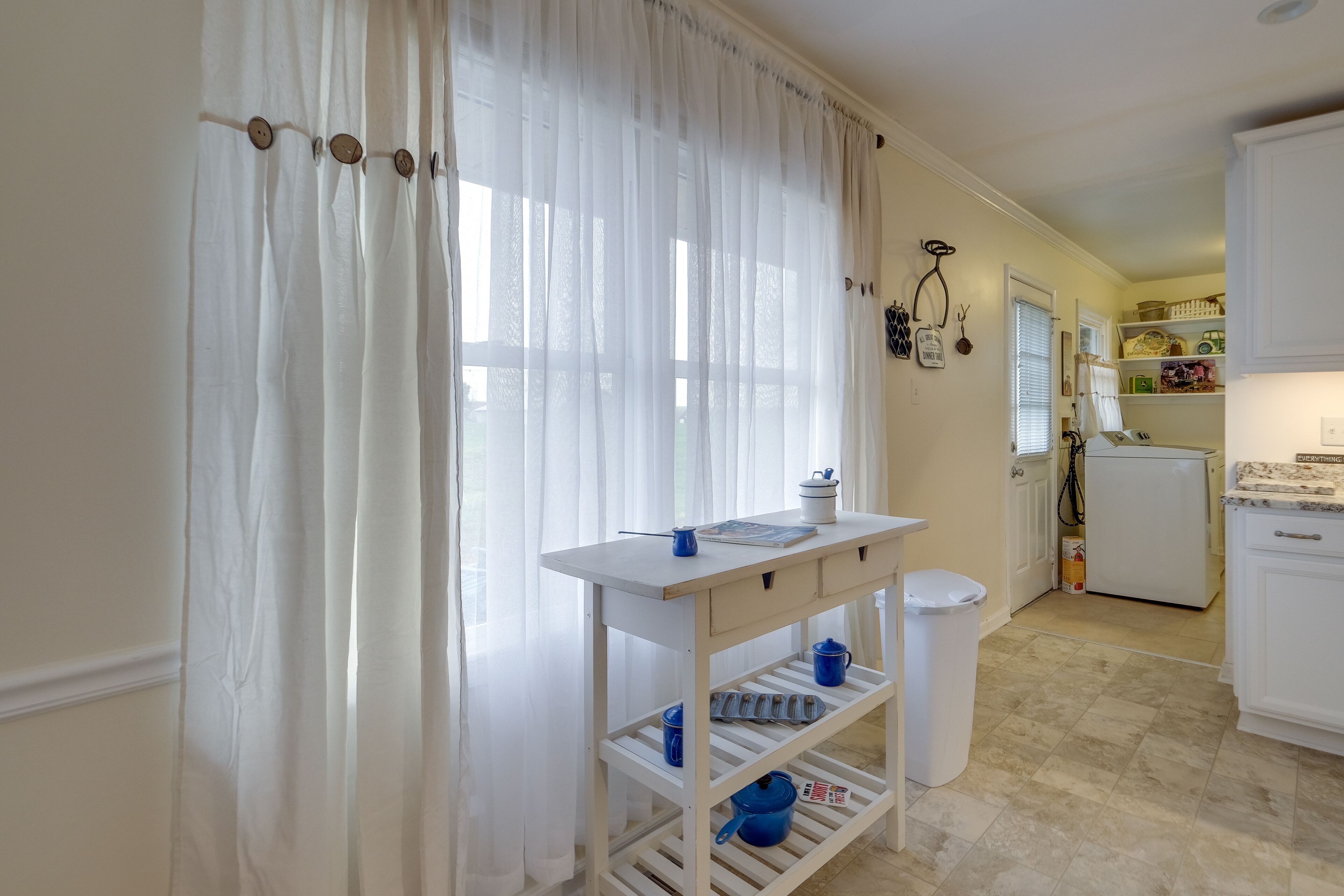 A kitchen with a white countertop, a sink, and a window with sheer curtains.