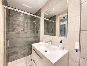 Un bagno moderno con cabina doccia in vetro, un mobile lavabo bianco con lavandino e uno specchio.