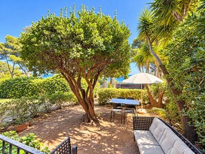 A garden area with a table and chairs, a bench, and a large tree providing shade.