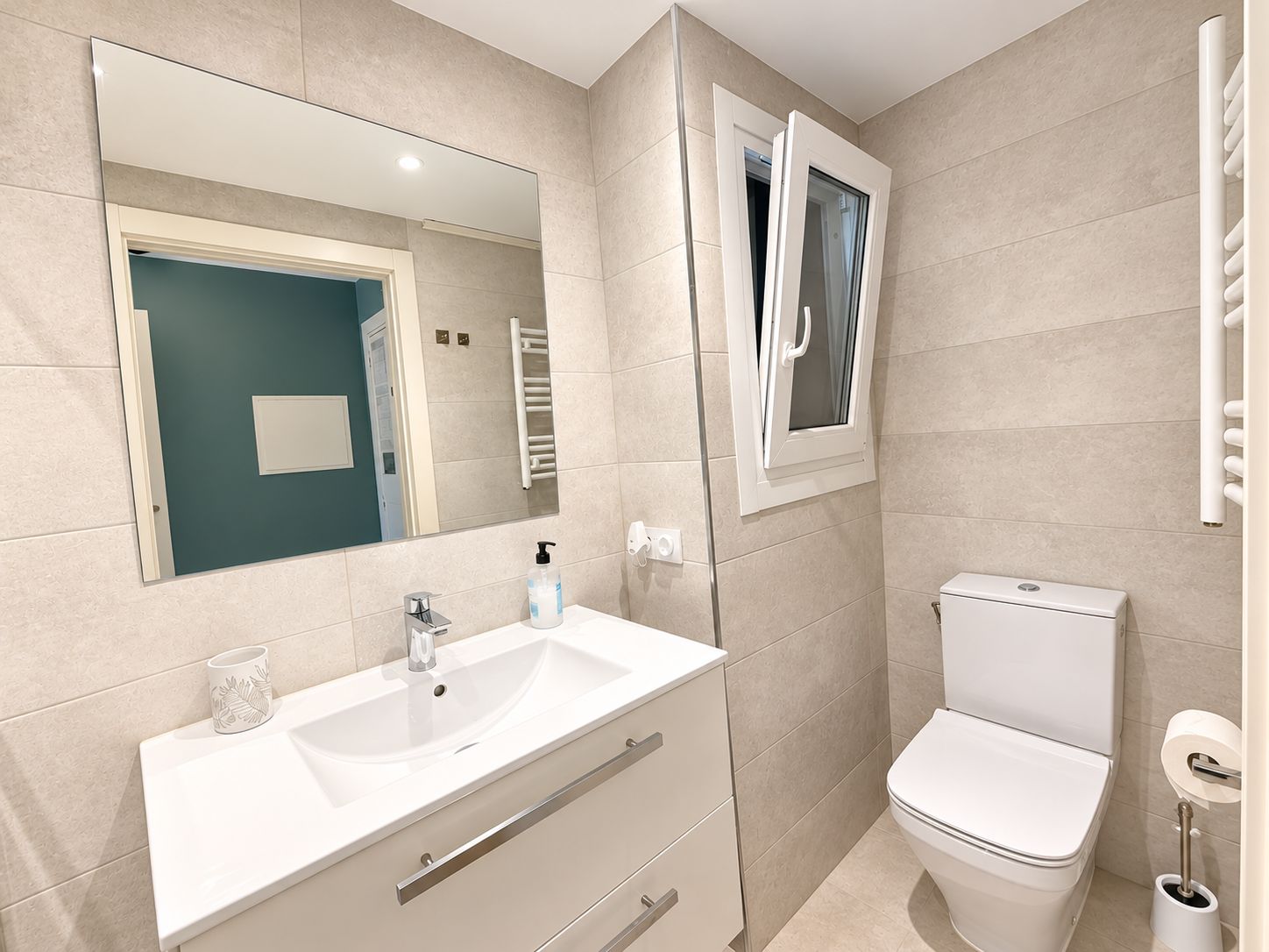 Un baño moderno con lavamanos, espejo, inodoro y toallero.