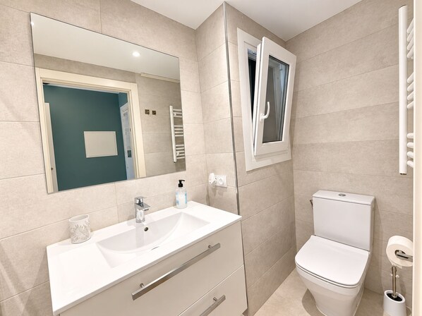 A modern bathroom with a sink, mirror, toilet, and towel rack.