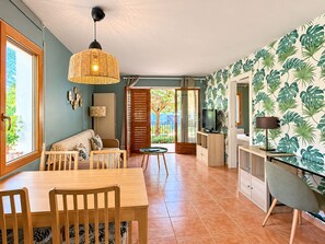 Una stanza con un tavolo da pranzo, sedie, un divano, una televisione e una parete decorata con un motivo a foglia tropicale.