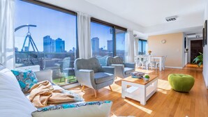 Ein modernes Wohnzimmer mit Stadtblick, ausgestattet mit einer Couch, Sesseln, einem Couchtisch und einem Essbereich.