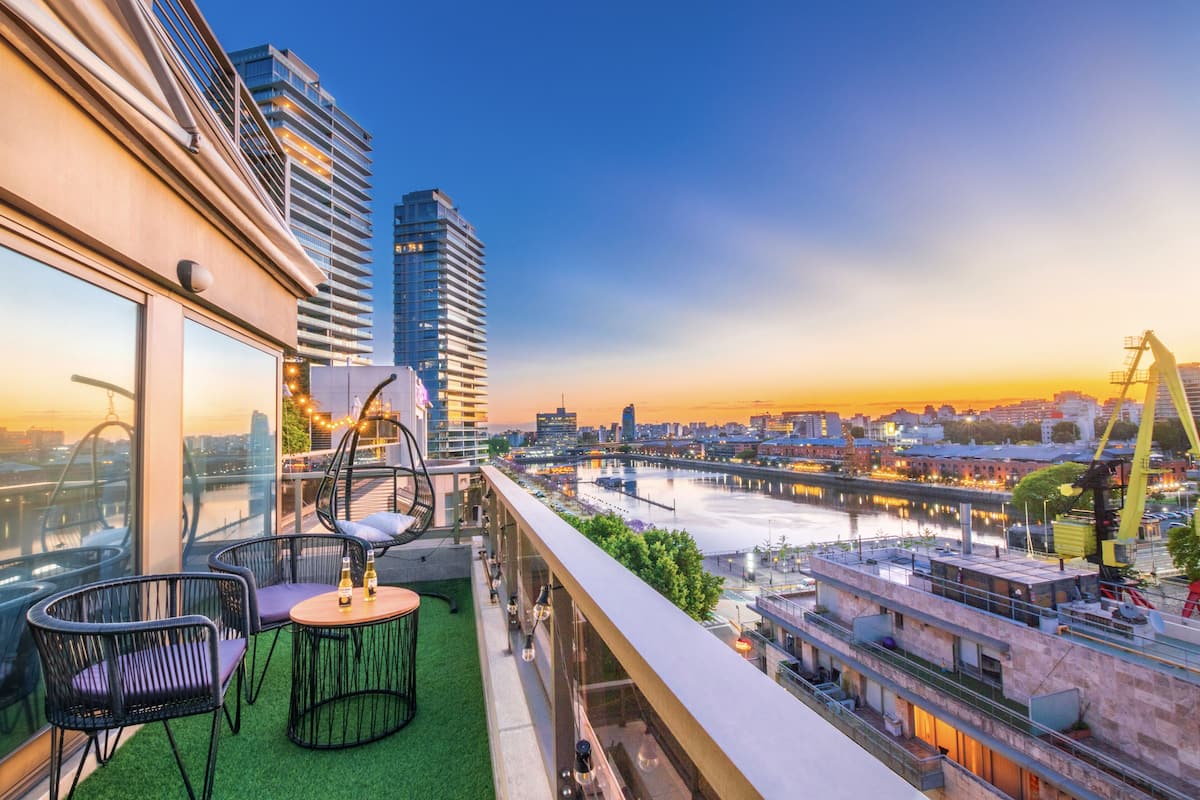 Un balcón con vistas a un paisaje urbano, incluyendo un río y un puente, y una mesa con sillas.