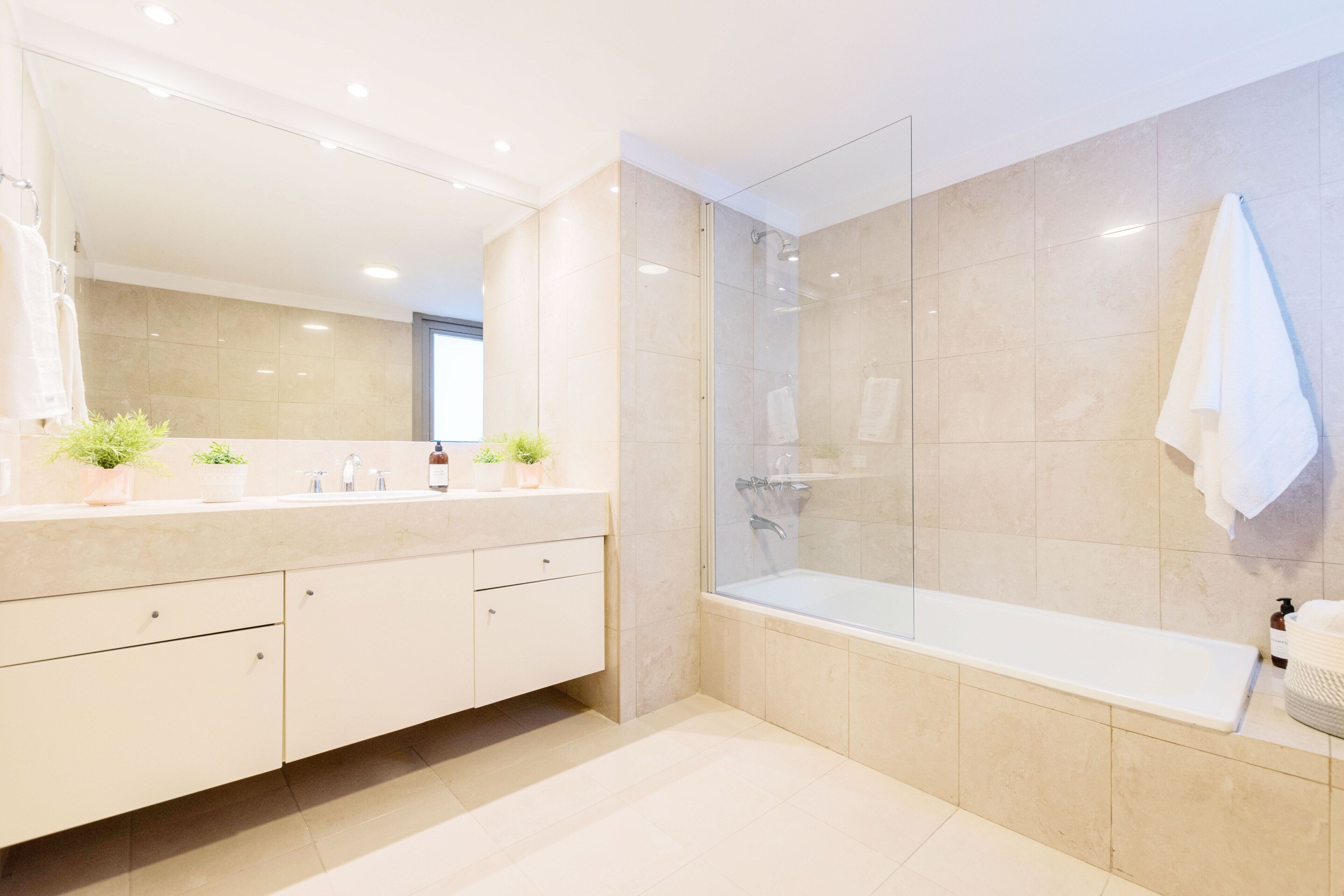 A modern bathroom with a glass-enclosed shower, a large mirror, and a bathtub.