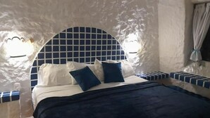 Een slaapkamer met een geruit hoofdeinde, een bed met wit- en blauwe beddengoed, en een raam met gordijnen.