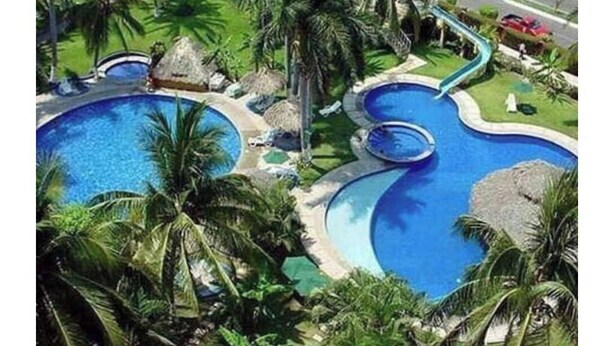 Een resort met diverse zwembaden, omgeven door palmbomen en hutten met rieten daken.