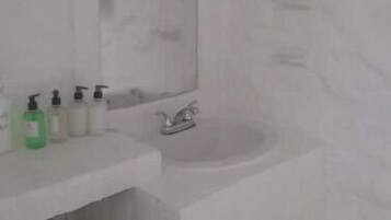 Ein Badezimmer mit einem weißen Waschbecken, einem Spiegel und einer Badewanne. Auf dem Waschbecken befinden sich Toilettenartikel.