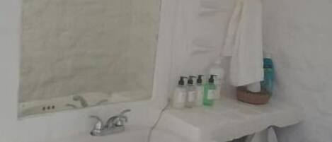 Un baño con un lavabo blanco, un espejo y un inodoro. Hay artículos de aseo en el lavabo y una toalla colgada en la pared.