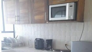 Een keuken met houten kastjes, een magnetron, een koffiezetapparaat en een koelkast.