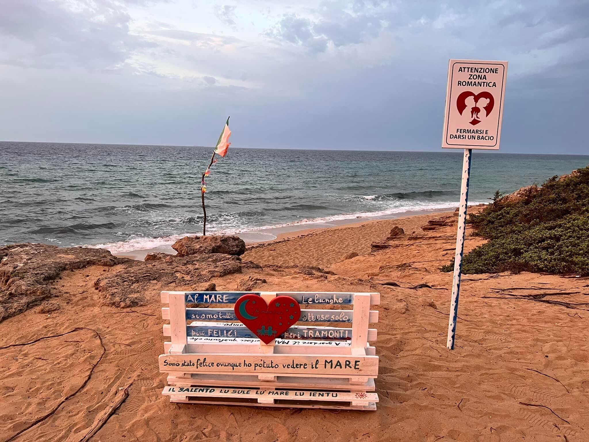 Une plage avec un panneau en bois portant plusieurs messages, un drapeau et un panneau d’avertissement.